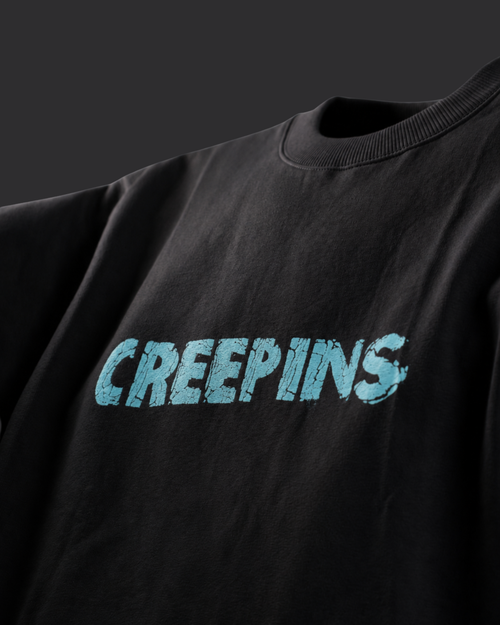 A close-up of a black crewneck sweatshirt featuring the word 'CREEPINS' printed across the chest in a distressed light blue font.