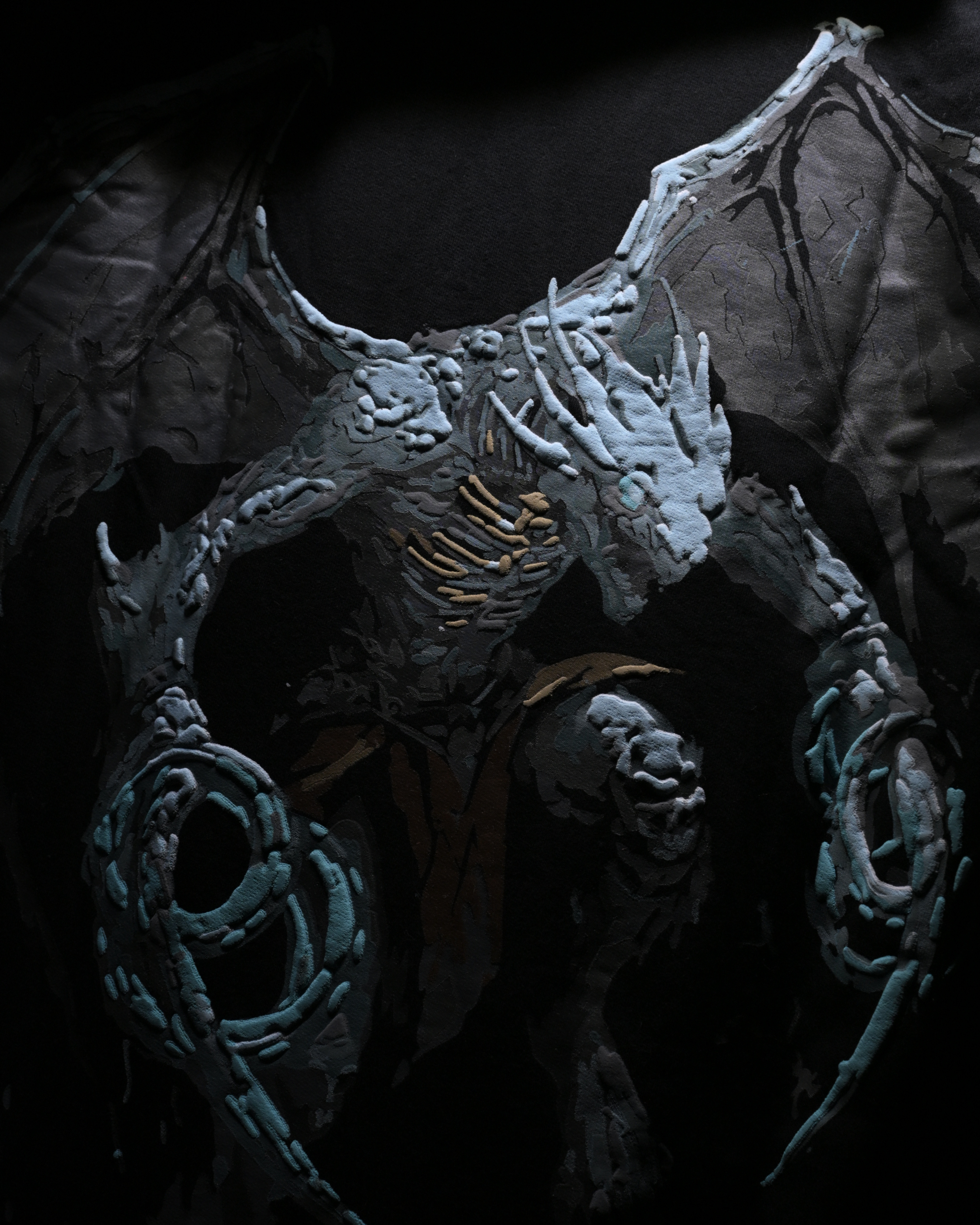 A dark fantasy creature sculpture or collectible figure with large bat-like wings, textured gray skin, sharp claws, and teal-blue coiled accessories, shown against a black background.