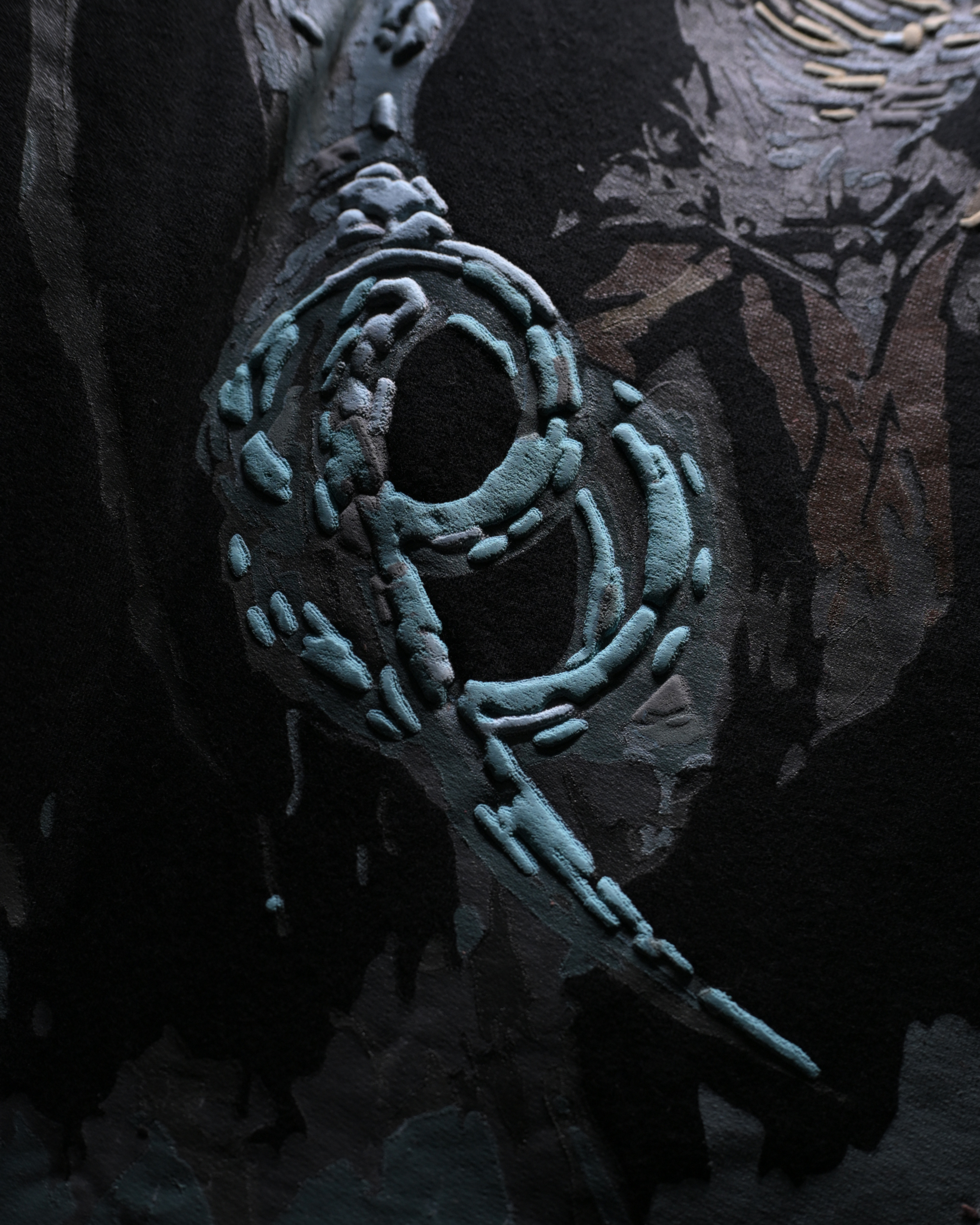 A close-up of a dark, textured surface featuring a prominent light blue-green abstract spiral or ring-like pattern against a black and charcoal background.